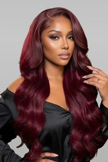 Woman with long, wavy, burgundy hair wearing a black top against a gray background