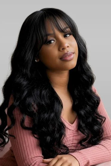 Woman with long black hair wearing a pink sweater against a gray background